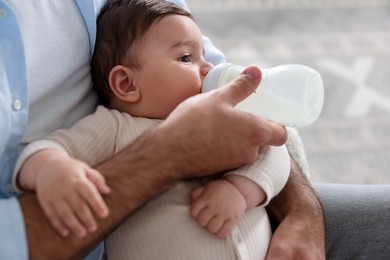 Photo of Father feeding his little baby with bottle on armchair at home, closeup