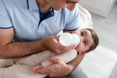 Photo of Father feeding his little baby with bottle on sofa at home, closeup