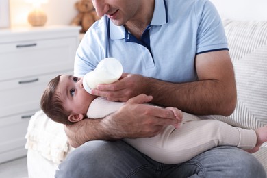 Photo of Father feeding his little baby with bottle on sofa at home, closeup