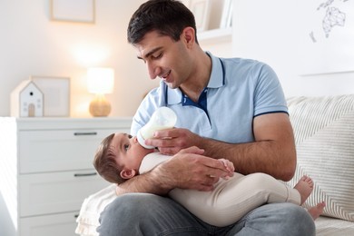 Photo of Father feeding his little baby with bottle on sofa at home