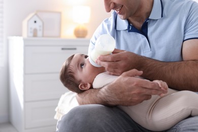 Photo of Father feeding his little baby with bottle on sofa at home, closeup