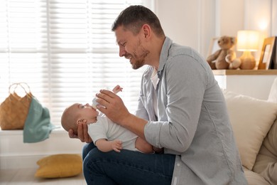 Photo of Father feeding his little baby with bottle on sofa at home