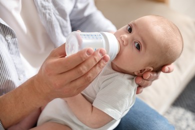 Photo of Father feeding his little baby with bottle on sofa at home, closeup