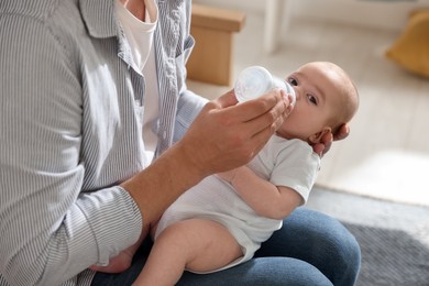 Photo of Father feeding his little baby with bottle on sofa at home, closeup