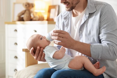 Photo of Father feeding his little baby with bottle on sofa at home, closeup