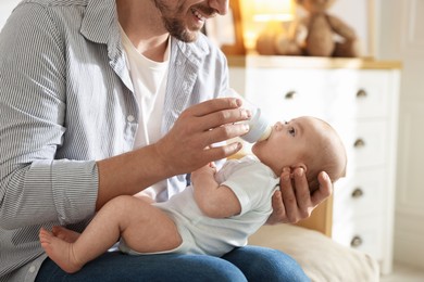 Photo of Father feeding his little baby with bottle on sofa at home, closeup