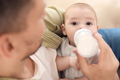 Photo of Father feeding his little baby with bottle on sofa at home, closeup