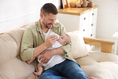 Photo of Father feeding his little baby with bottle on sofa at home. Space for text