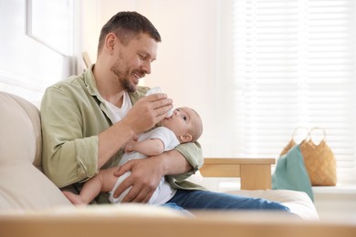 Photo of Father feeding his little baby with bottle on sofa at home. Space for text