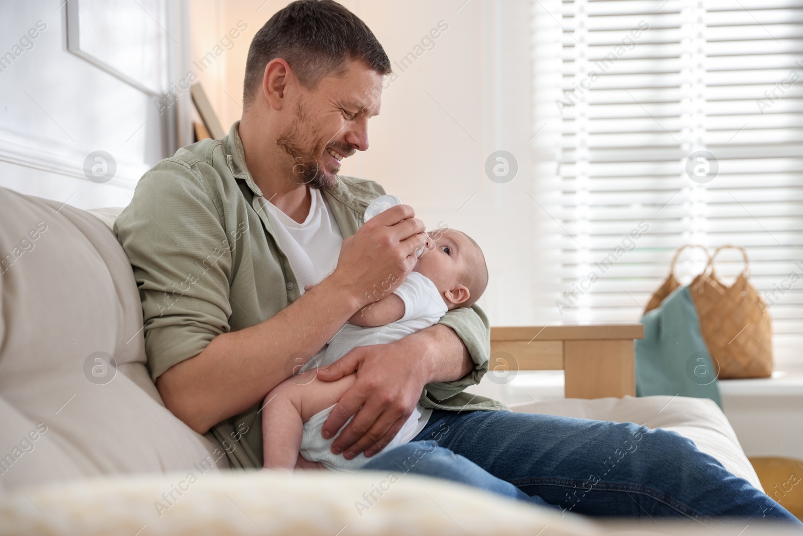 Father feeding his little baby with bottle on sofa at home. Space for text Photo of Father feeding his little baby with bottle on sofa at home. Space for text