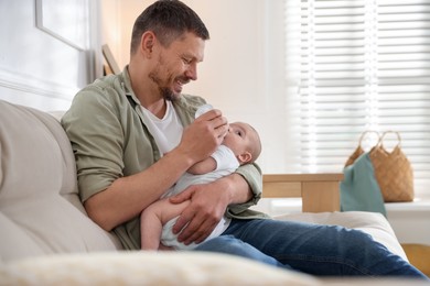 Photo of Father feeding his little baby with bottle on sofa at home. Space for text