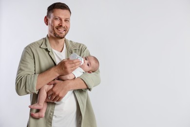 Photo of Father feeding his little baby with bottle on light background. Space for text