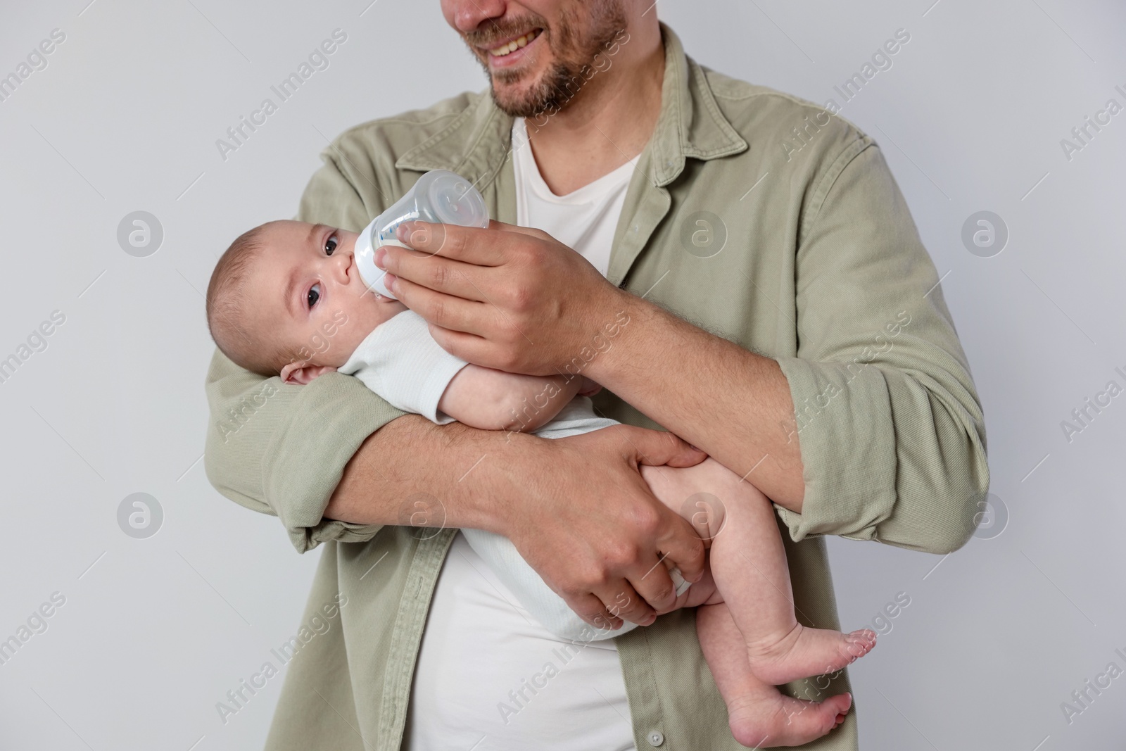 Father feeding his little baby with bottle on light background, closeup Photo of Father feeding his little baby with bottle on light background, closeup