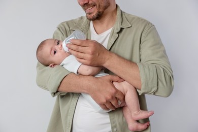 Photo of Father feeding his little baby with bottle on light background, closeup