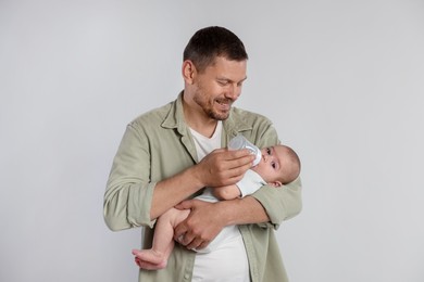 Photo of Father feeding his little baby with bottle on light background