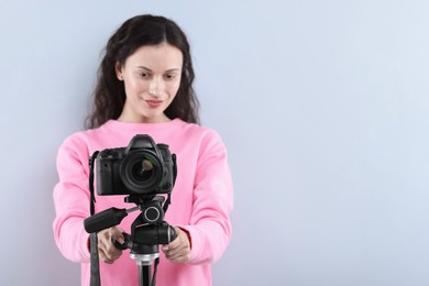 Photo of Woman with professional video camera on light grey background, selective focus. Space for text