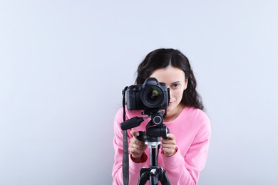 Photo of Woman with professional video camera on light grey background, space for text