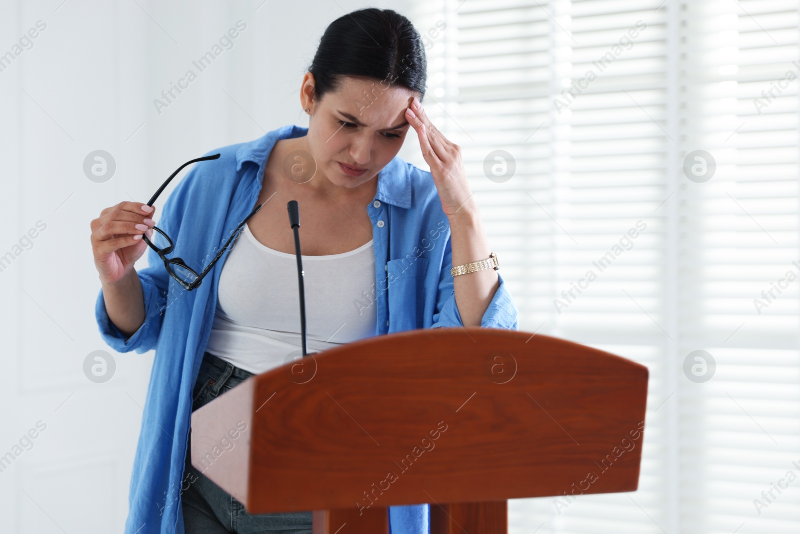 Fear of public speaking. Nervous woman with microphone at lectern indoors Photo of Fear of public speaking. Nervous woman with microphone at lectern indoors