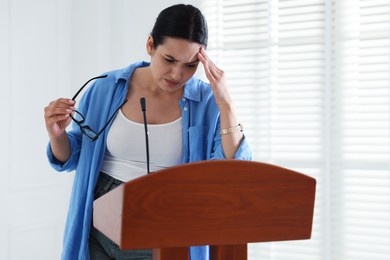 Photo of Fear of public speaking. Nervous woman with microphone at lectern indoors