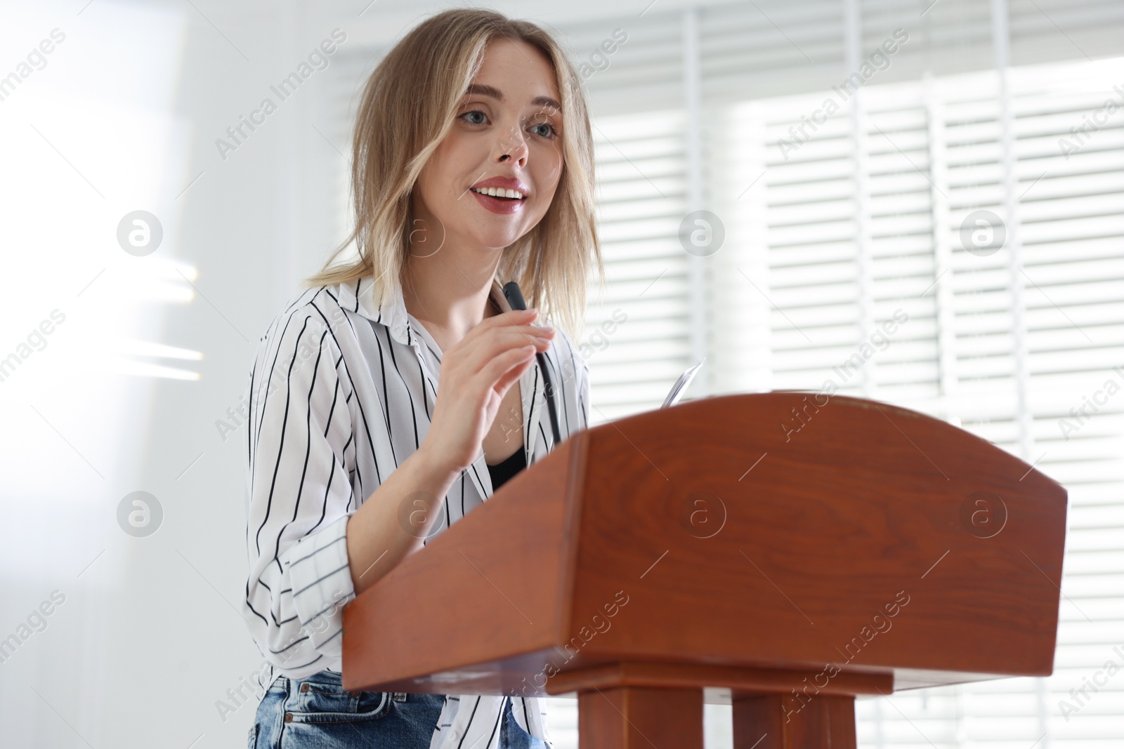 Woman giving public speech with microphone at lectern indoors Photo of Woman giving public speech with microphone at lectern indoors