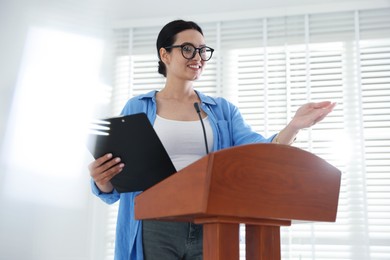 Photo of Woman giving public speech with microphone at lectern indoors