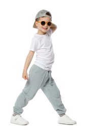 Photo of Happy little boy in sunglasses and baseball hat dancing on white background