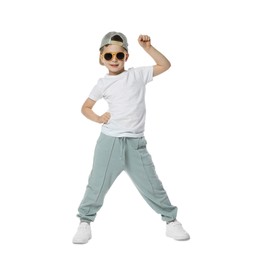 Photo of Happy little boy in sunglasses and baseball hat dancing on white background