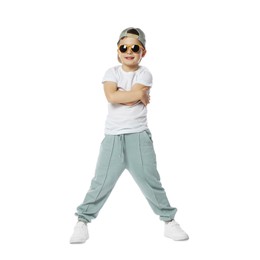 Photo of Happy little boy in sunglasses and baseball hat dancing on white background