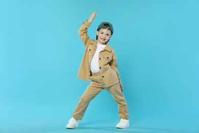 Photo of Happy little boy in baseball hat dancing on light blue background