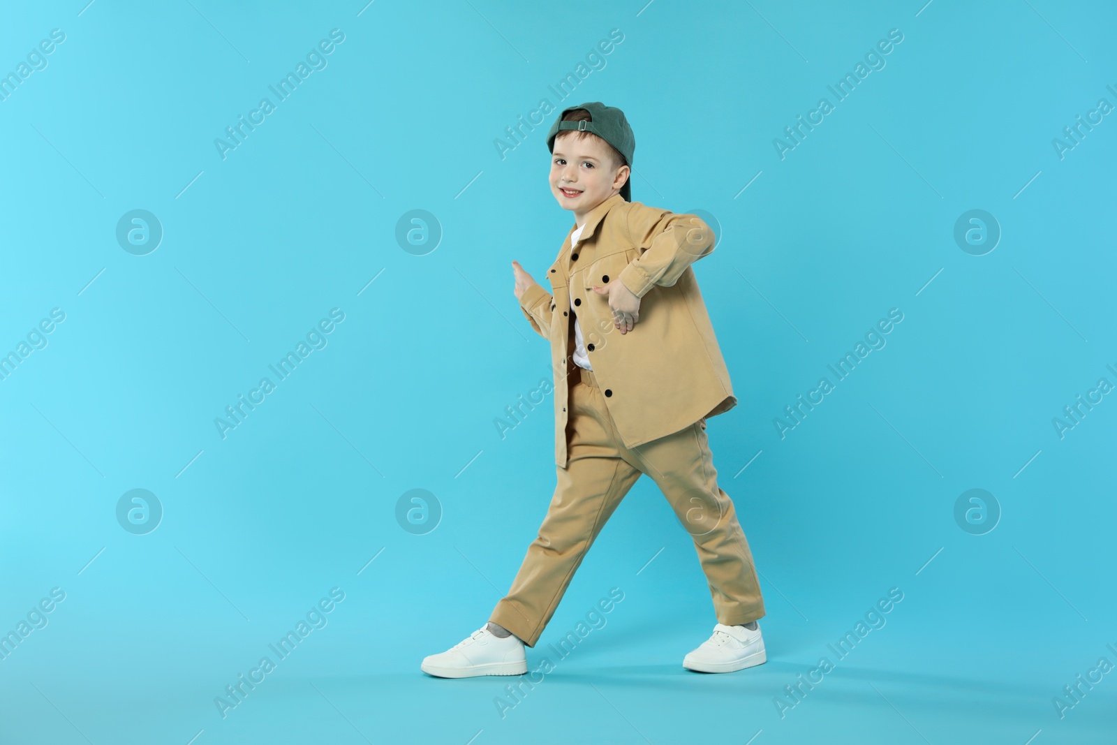Happy little boy in baseball hat dancing on light blue background. Space for text Photo of Happy little boy in baseball hat dancing on light blue background. Space for text