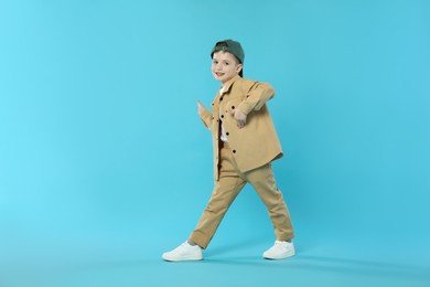 Photo of Happy little boy in baseball hat dancing on light blue background. Space for text