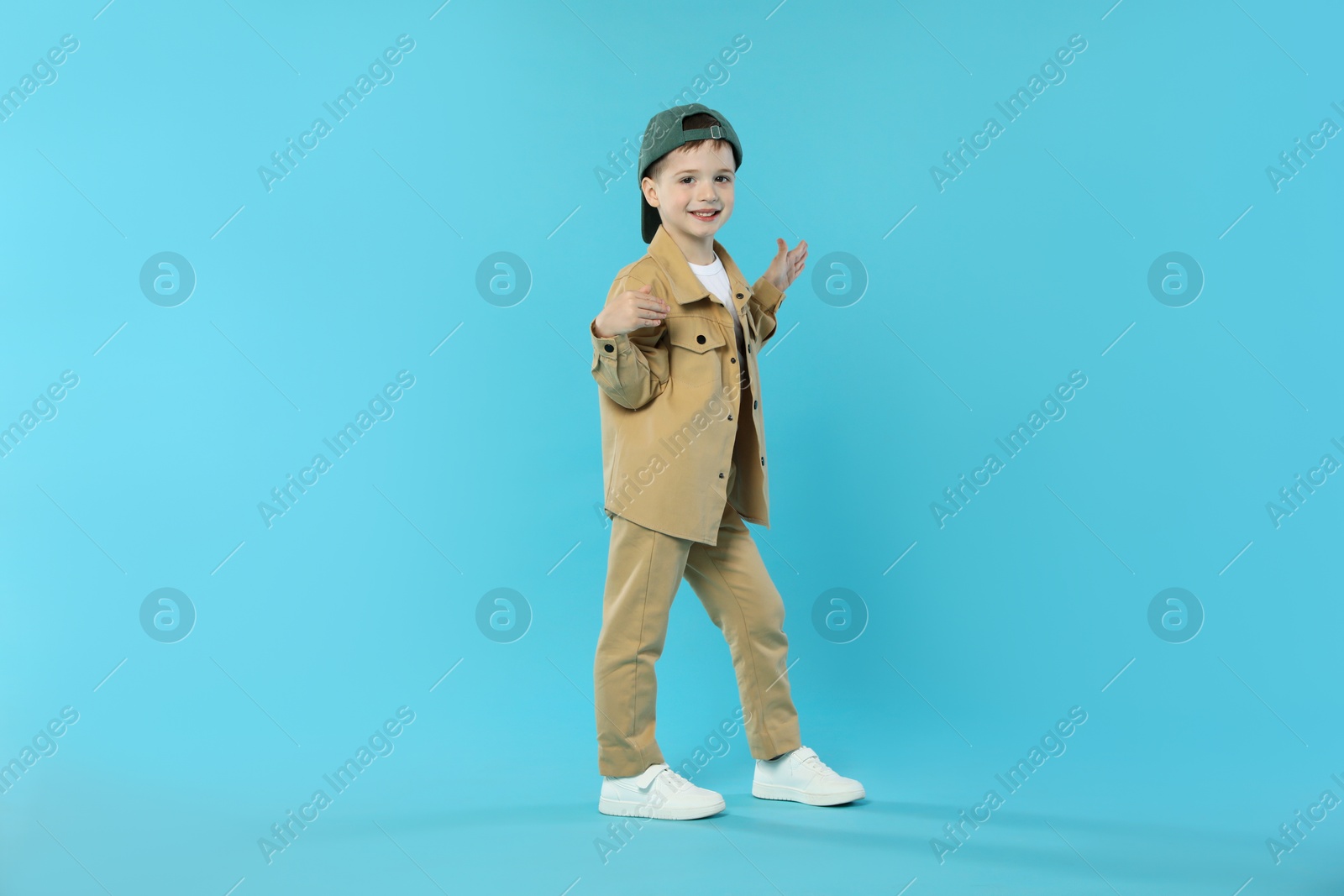 Happy little boy in baseball hat dancing on light blue background. Space for text Photo of Happy little boy in baseball hat dancing on light blue background. Space for text