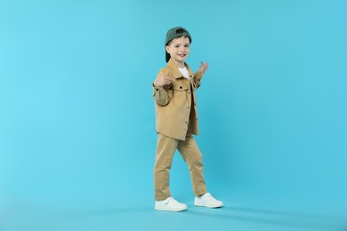 Photo of Happy little boy in baseball hat dancing on light blue background. Space for text