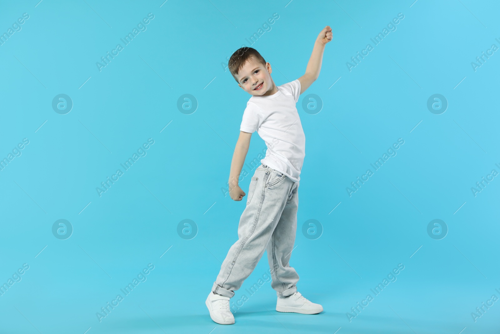 Happy little boy dancing on light blue background. Space for text Photo of Happy little boy dancing on light blue background. Space for text