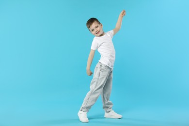 Photo of Happy little boy dancing on light blue background. Space for text
