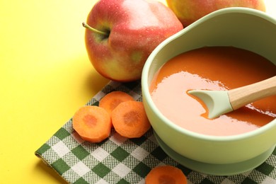 Photo of Baby food. Tasty puree in bowl and ingredients on yellow background, closeup