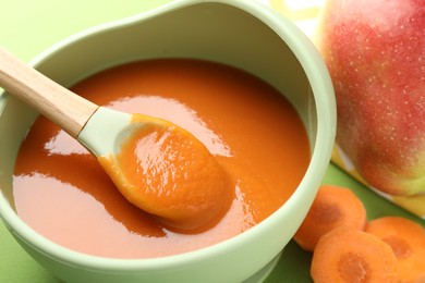 Photo of Baby food. Tasty puree in bowl and ingredients on green background, closeup