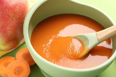 Photo of Baby food. Tasty puree in bowl and ingredients on green background, closeup