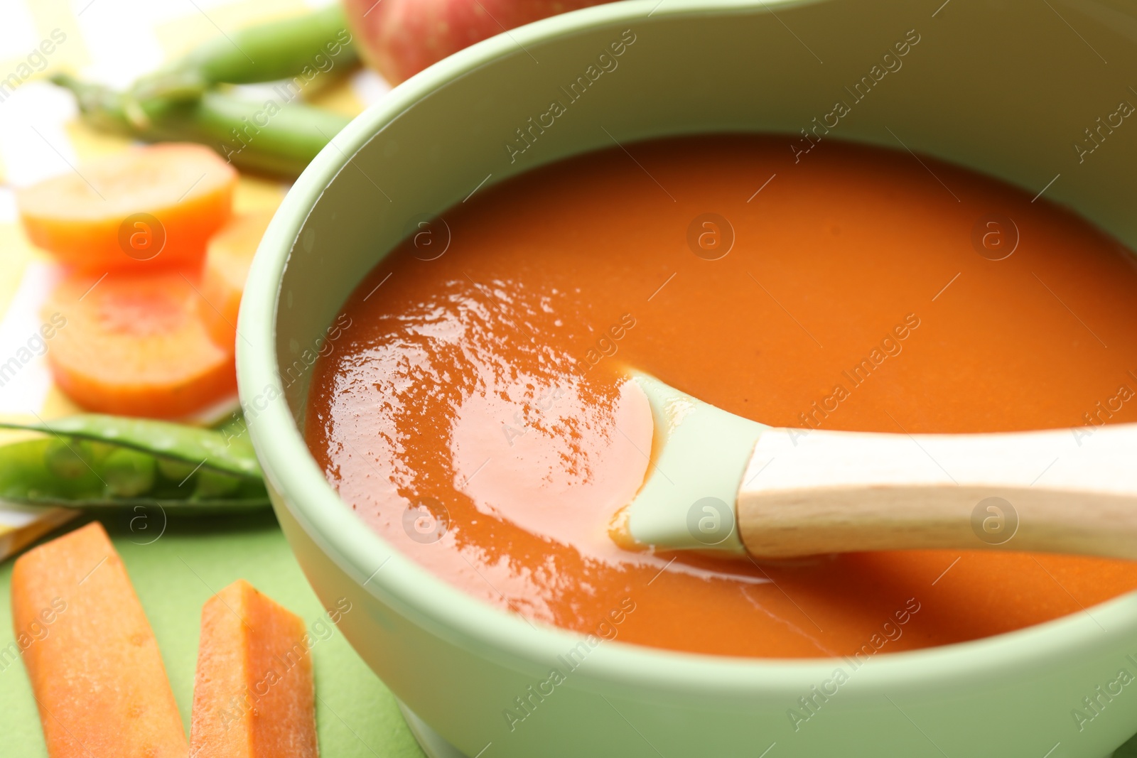 Baby food. Tasty puree in bowl and ingredients on green background, closeup Photo of Baby food. Tasty puree in bowl and ingredients on green background, closeup