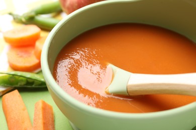 Photo of Baby food. Tasty puree in bowl and ingredients on green background, closeup