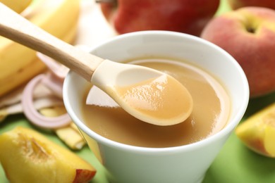 Photo of Baby food. Taking tasty puree with spoon on green background, closeup