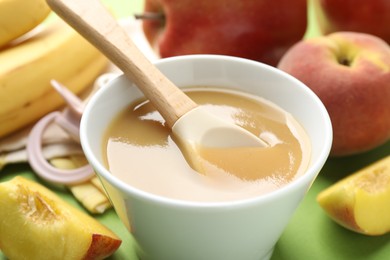 Photo of Baby food. Tasty puree in bowl and ingredients on green background, closeup