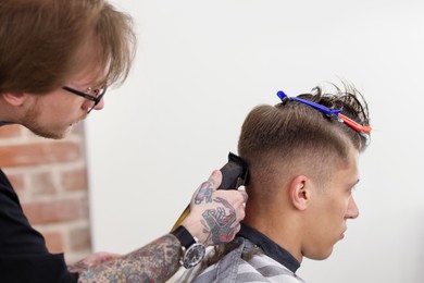 Photo of Professional barber making stylish haircut in barbershop, closeup