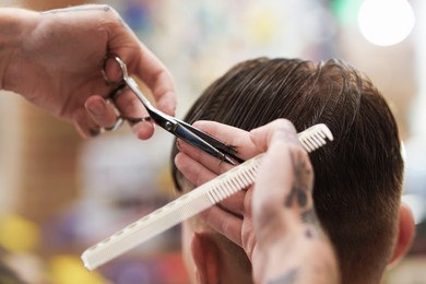 Photo of Professional barber cutting client's hair with scissors in barbershop, closeup