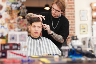 Photo of Professional barber making stylish haircut in barbershop