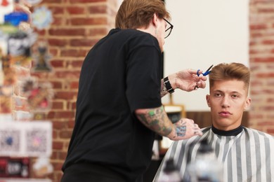 Photo of Professional barber cutting client's hair with scissors in barbershop