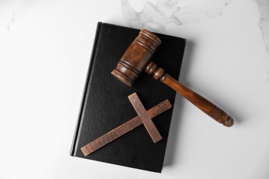 Photo of Judge's gavel, Bible and wooden cross on white marble table, top view