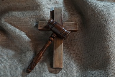 Photo of Judge's gavel and wooden cross on burlap fabric, top view