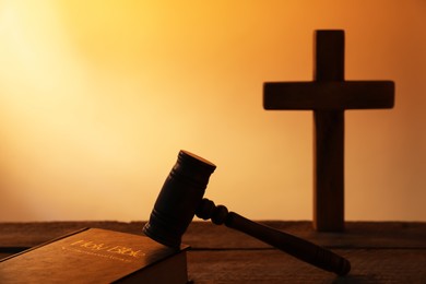 Photo of Judge's gavel, Bible and cross on wooden table against pale orange gradient background, closeup