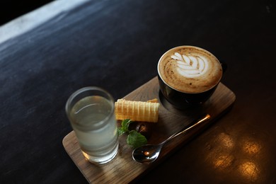 Photo of Cup of coffee, wafer and glass with water served on dark wooden table, above view